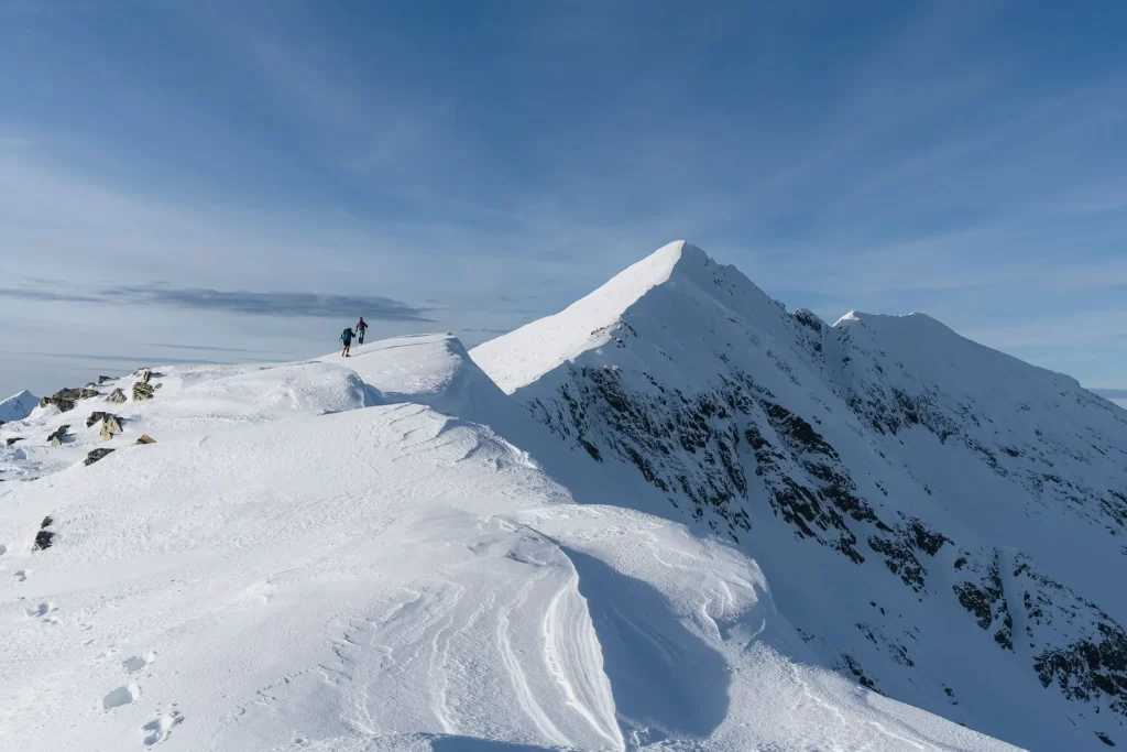 Two hikers approaching a sharp, snowy summit