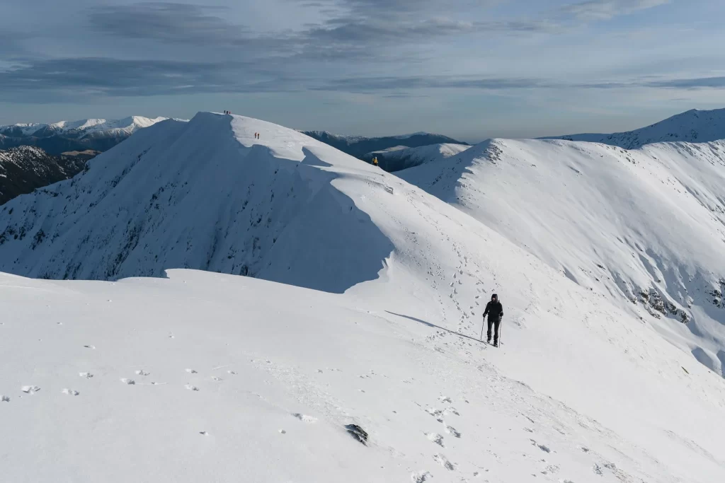 A solitary hiker walking along a snowy ridge with distant peaks