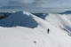 A solitary hiker walking along a snowy ridge with distant peaks