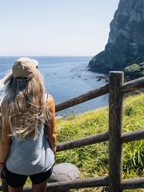 Woman facing Seongsan Ilchulbong’s coastline